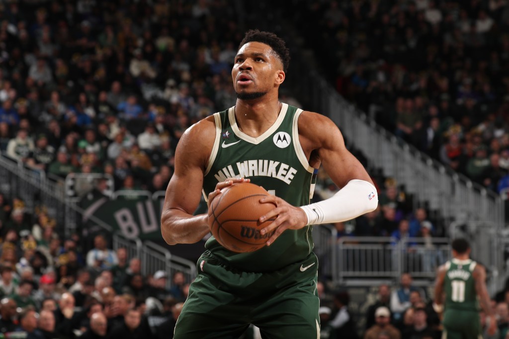 Giannis Antetokounmpo lleva una camiseta verde de los Milwaukee Bucks y una pelota de baloncesto en la mano.