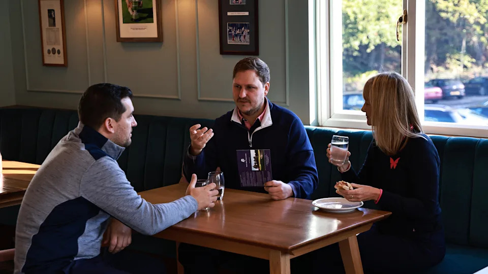 Nick Bonfield, Alison Root y Sam De'Ath toman una copa en la casa club después de la ronda y discuten sus puntuaciones.